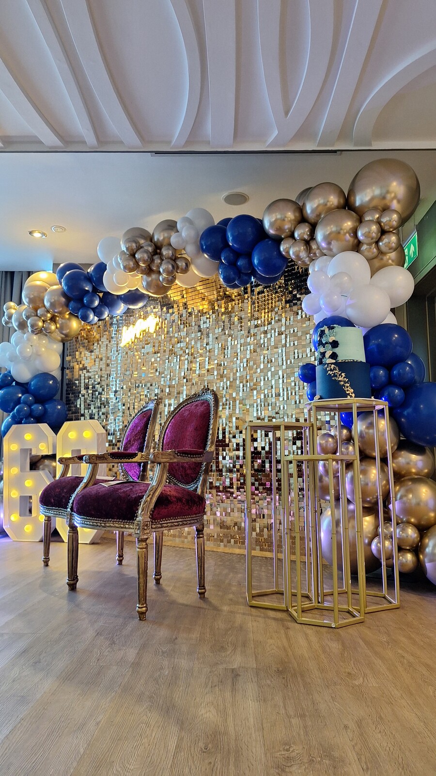 Gold sequin wall styled with a velvet chair, cake and gold stands