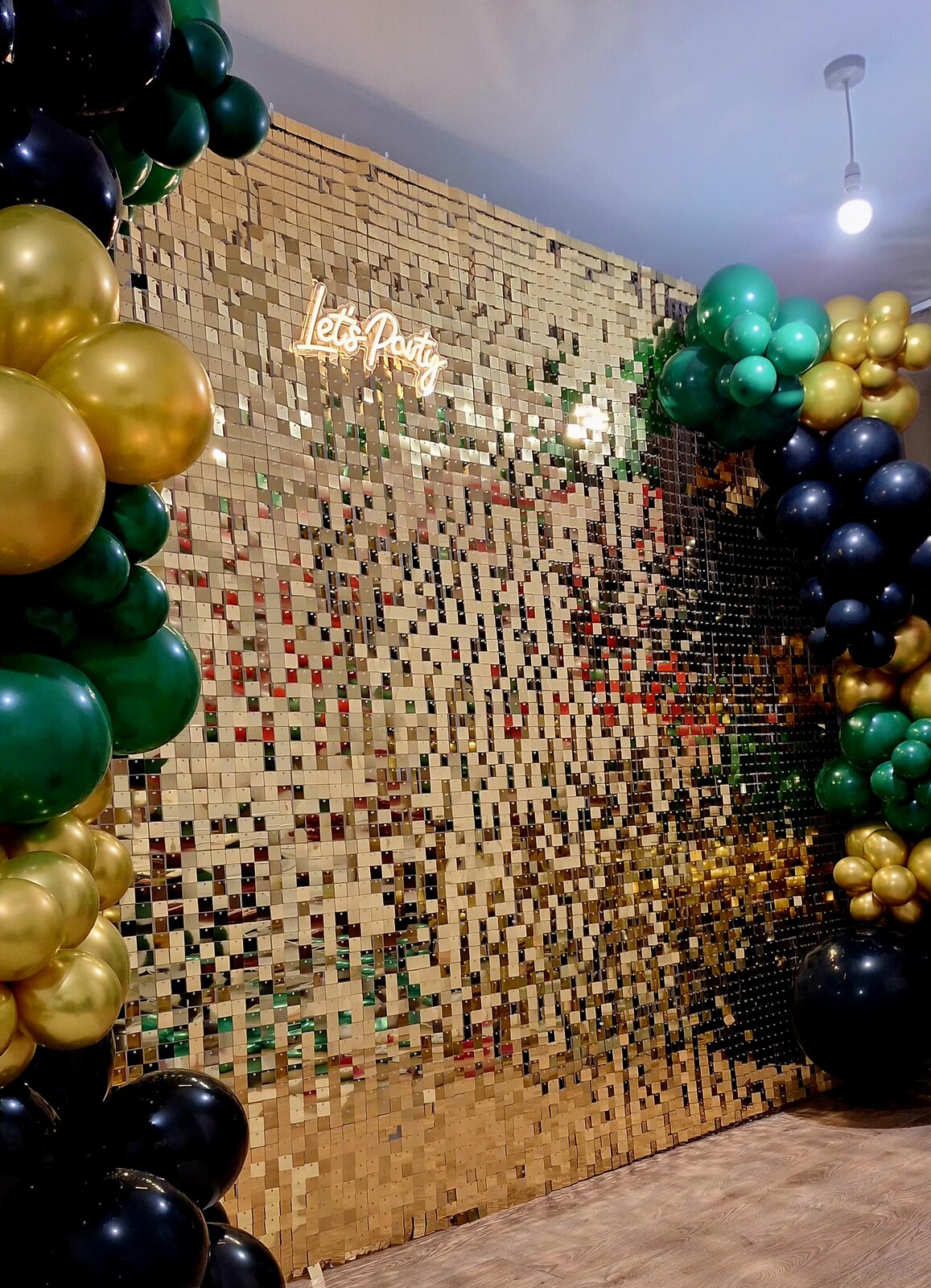 Gold sequin wall with Let's Party neon sign and green and gold balloons