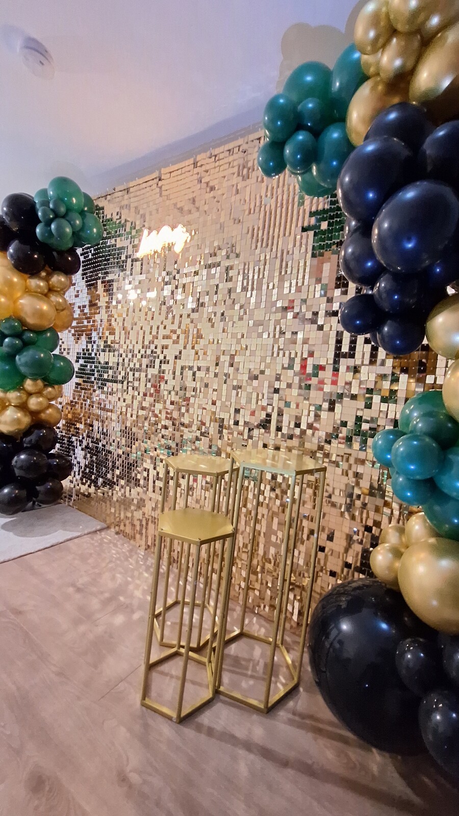 Gold shimmer wall with golden plinths and emerald balloon garland
